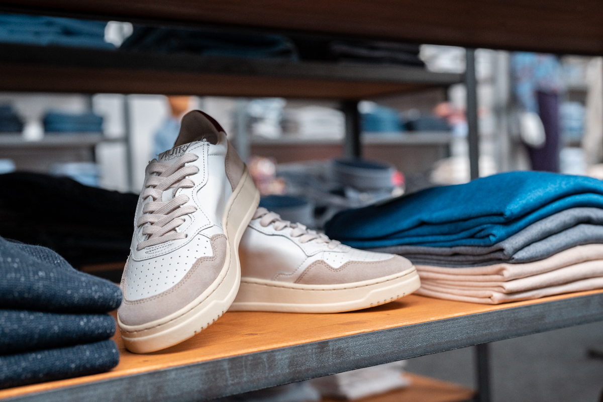 Klassische beige-weiße Autry Medalist Sneaker auf einem Regal zwischen Kleidungsstücken